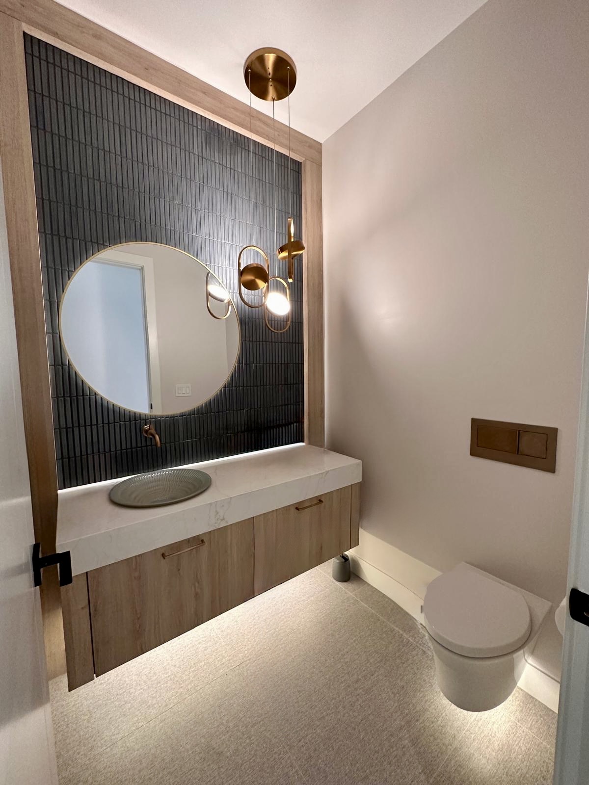 A powder room with ribbed blue tile, a round mirror and a floating oak vanity.