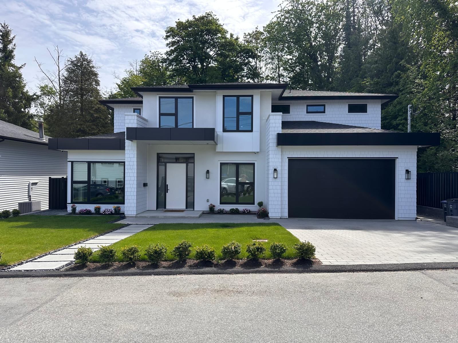 The front of the house as built: white shingle walls, black window frames and a black garage door.