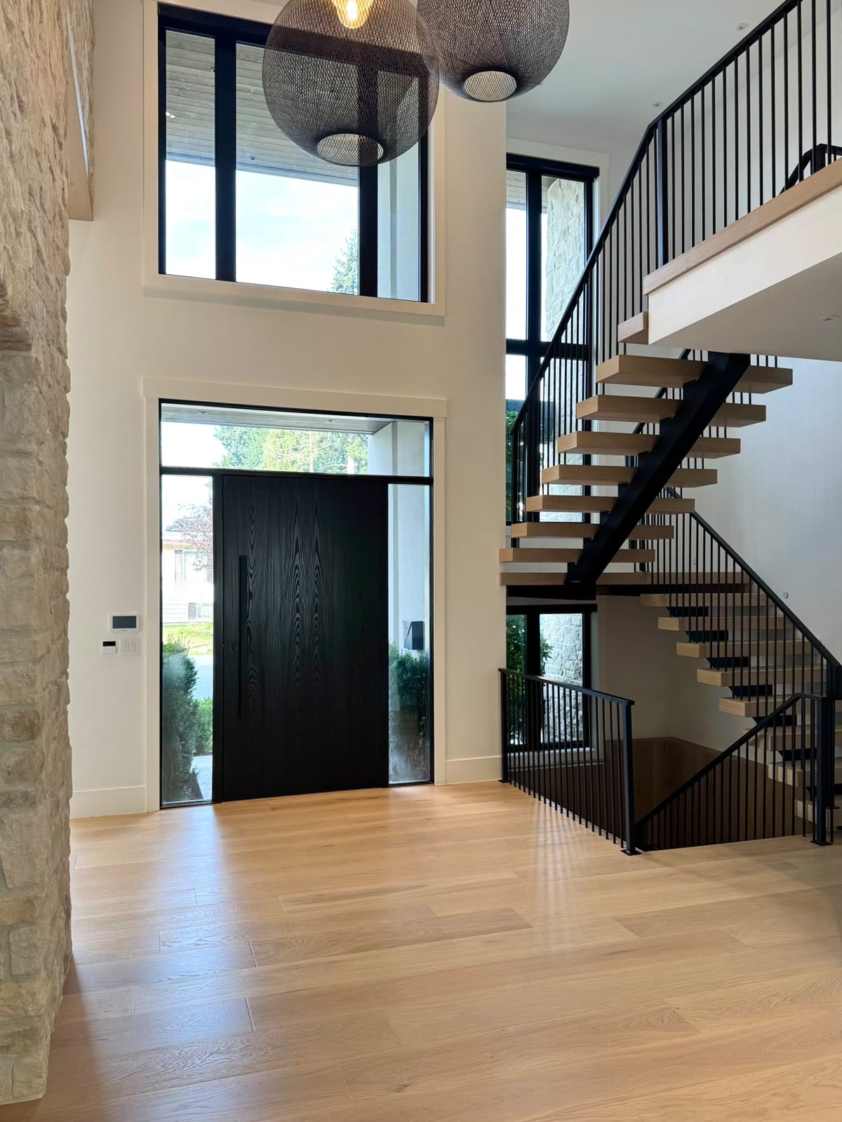 The entry: a tall black door with glass beside it, a stone wall at the left and an oak stair with a black steel rail at the right.