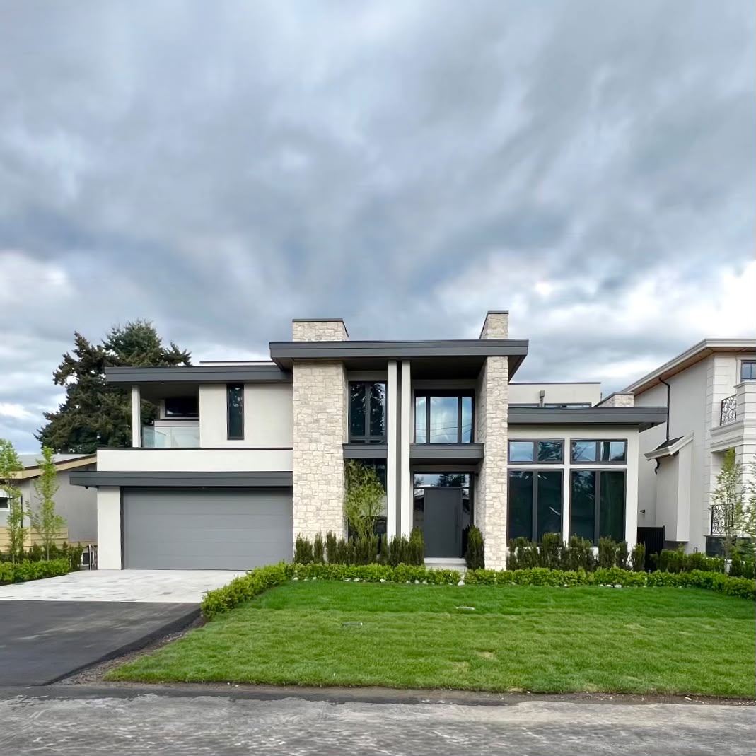 The front of the house: stone-clad columns, pale rendered walls, black window frames and a double garage, over a lawn edged with a low hedge.