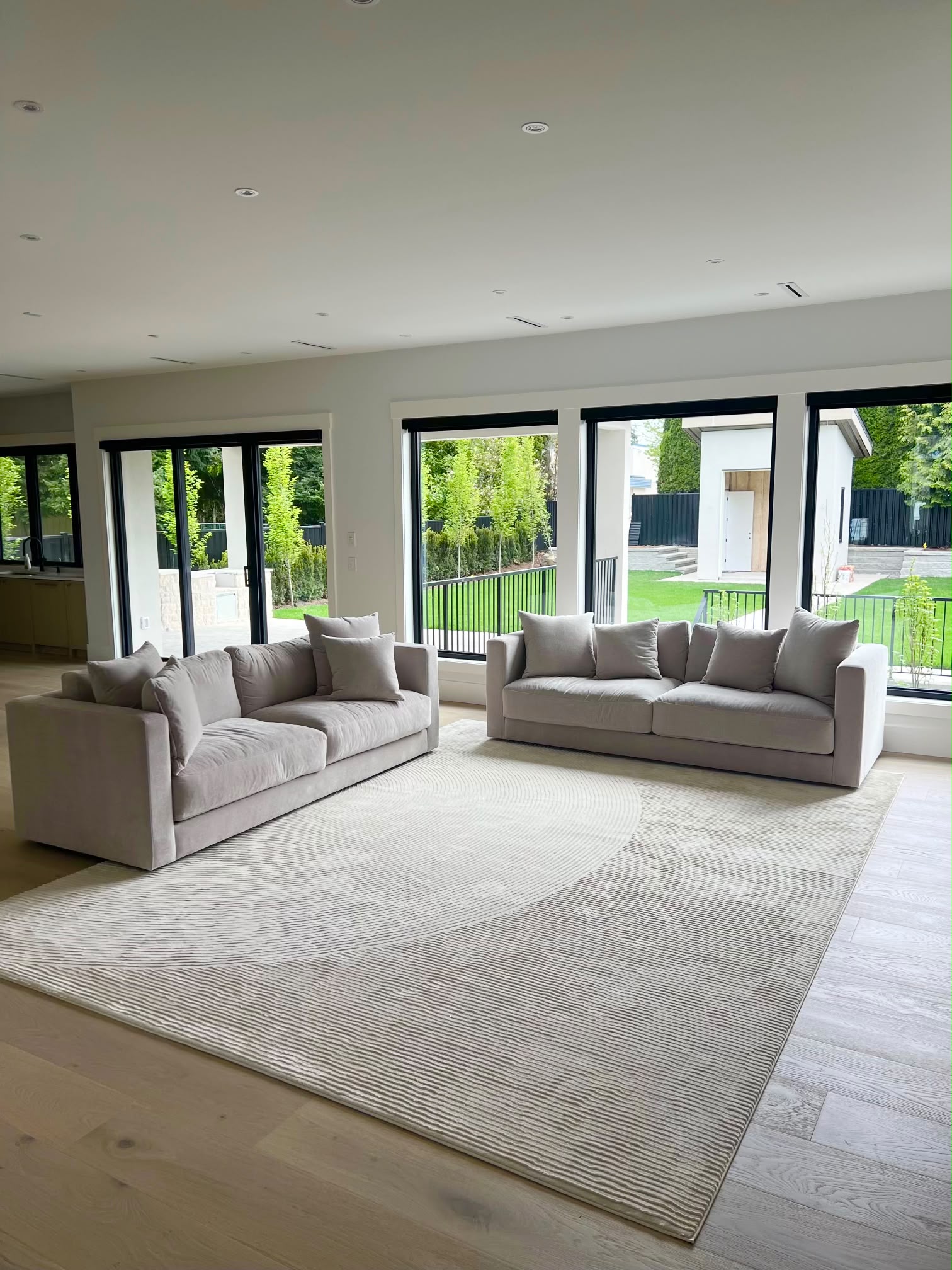 The open living area: two grey sofas on a patterned rug in front of tall black-framed windows onto the lawn.