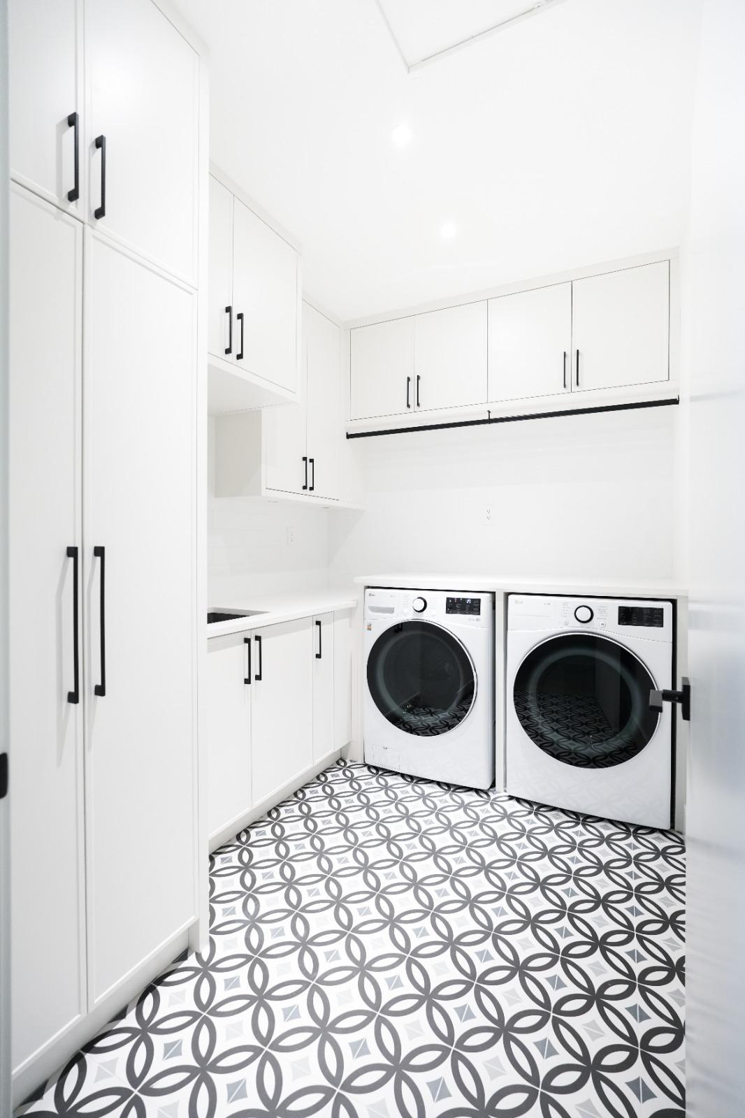 A laundry with white cabinets and a patterned tile floor.