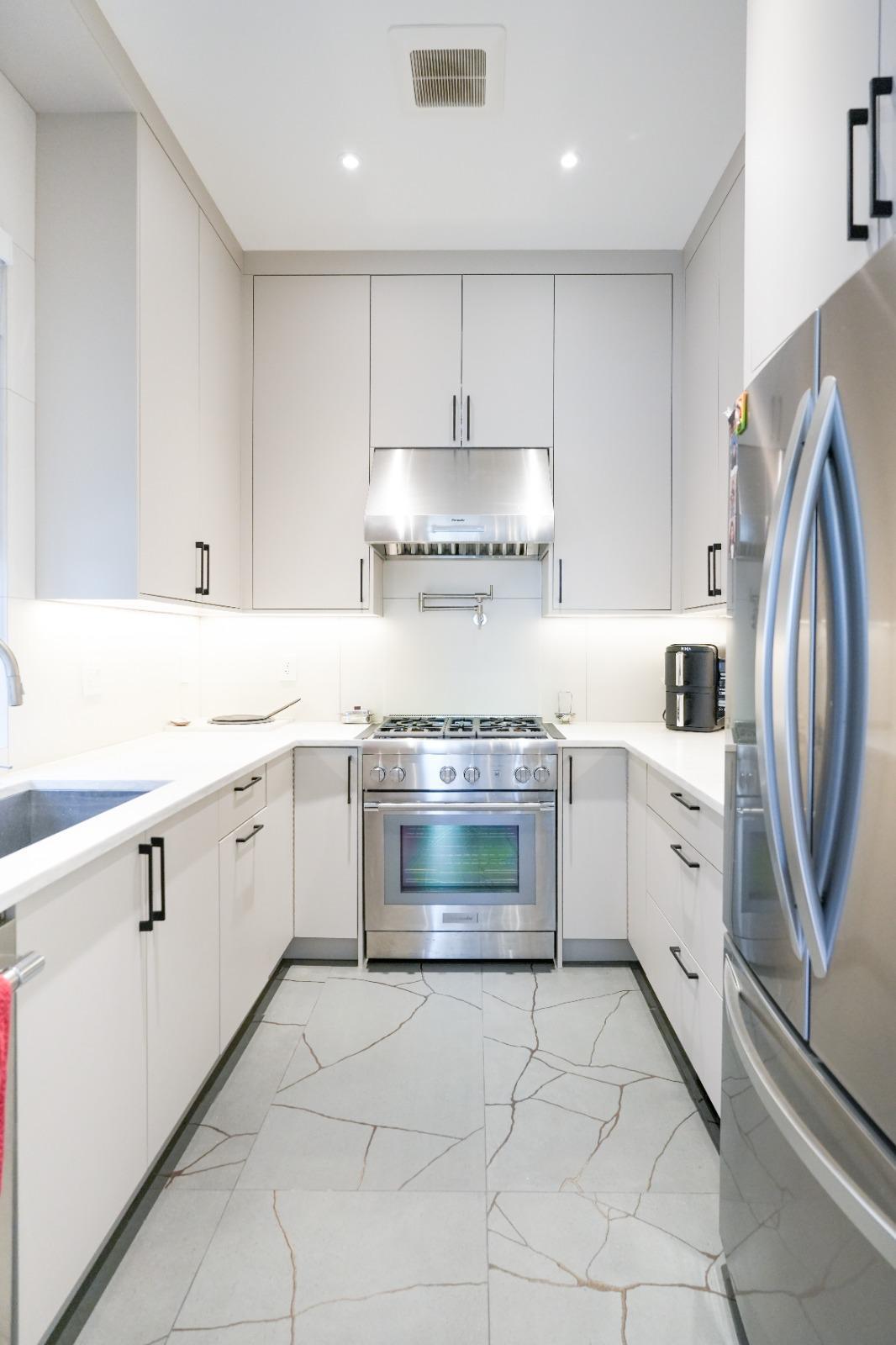 A small white working kitchen with a stainless range and hood.