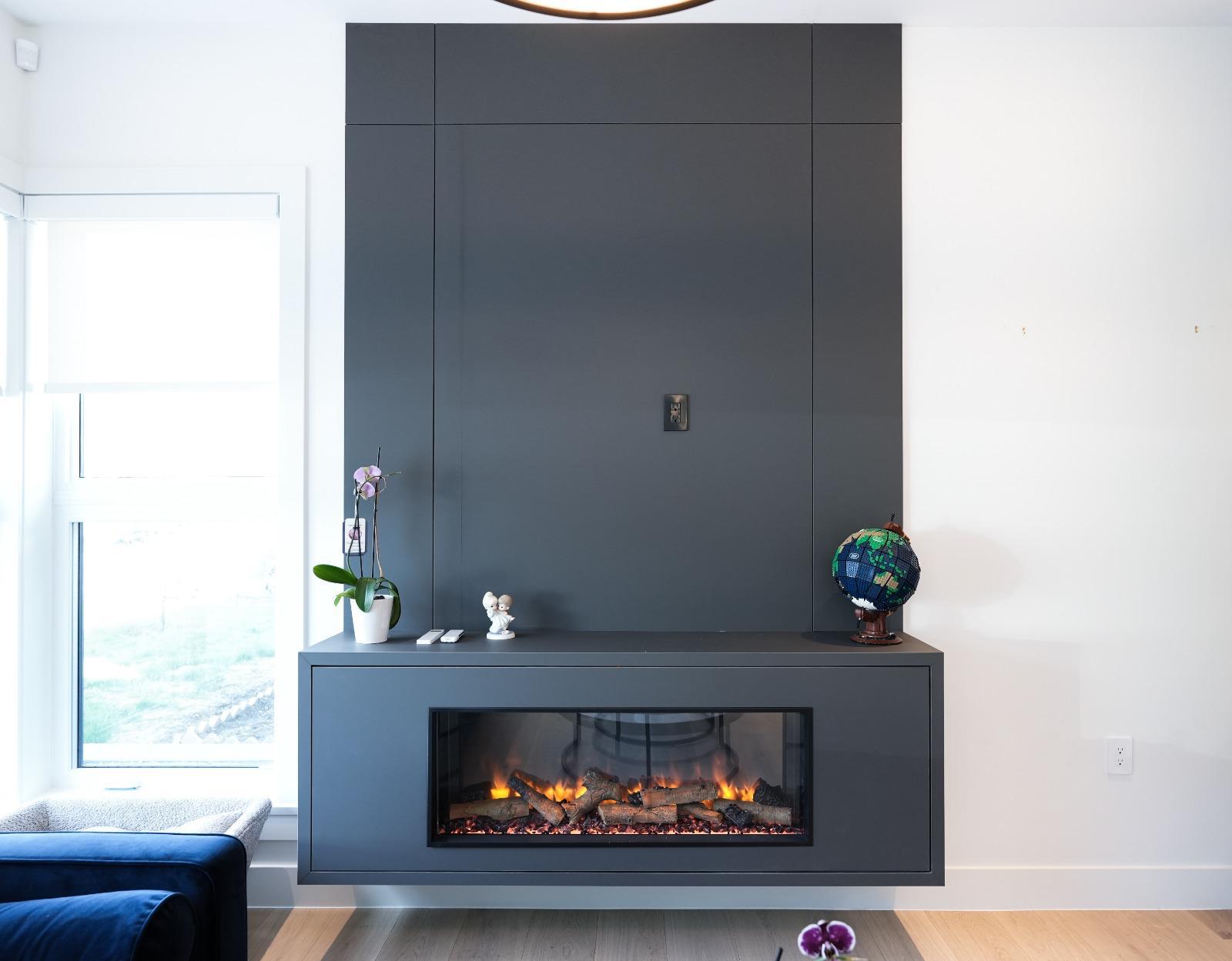 A linear fireplace set in a full-height charcoal panel beside a tall window.