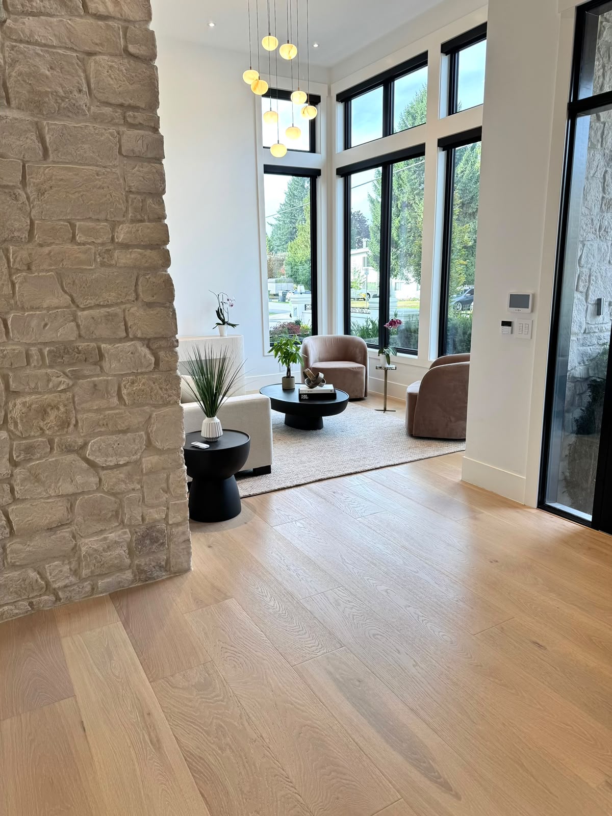 A sitting room beside the stone wall: two blush armchairs and a black coffee table under a cluster of round pendant lights, by tall windows.